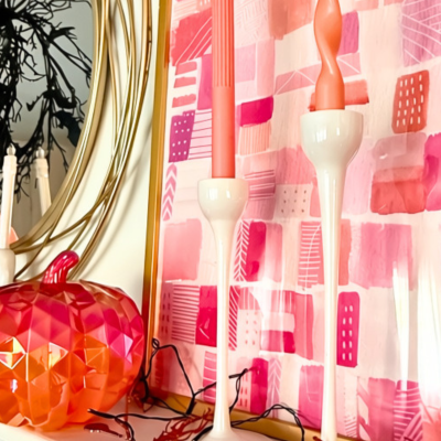 Halloween mantel with a pink and orange pumpkin, white ghost candelabra, black bat wreath, pink artwork, and taper candles.